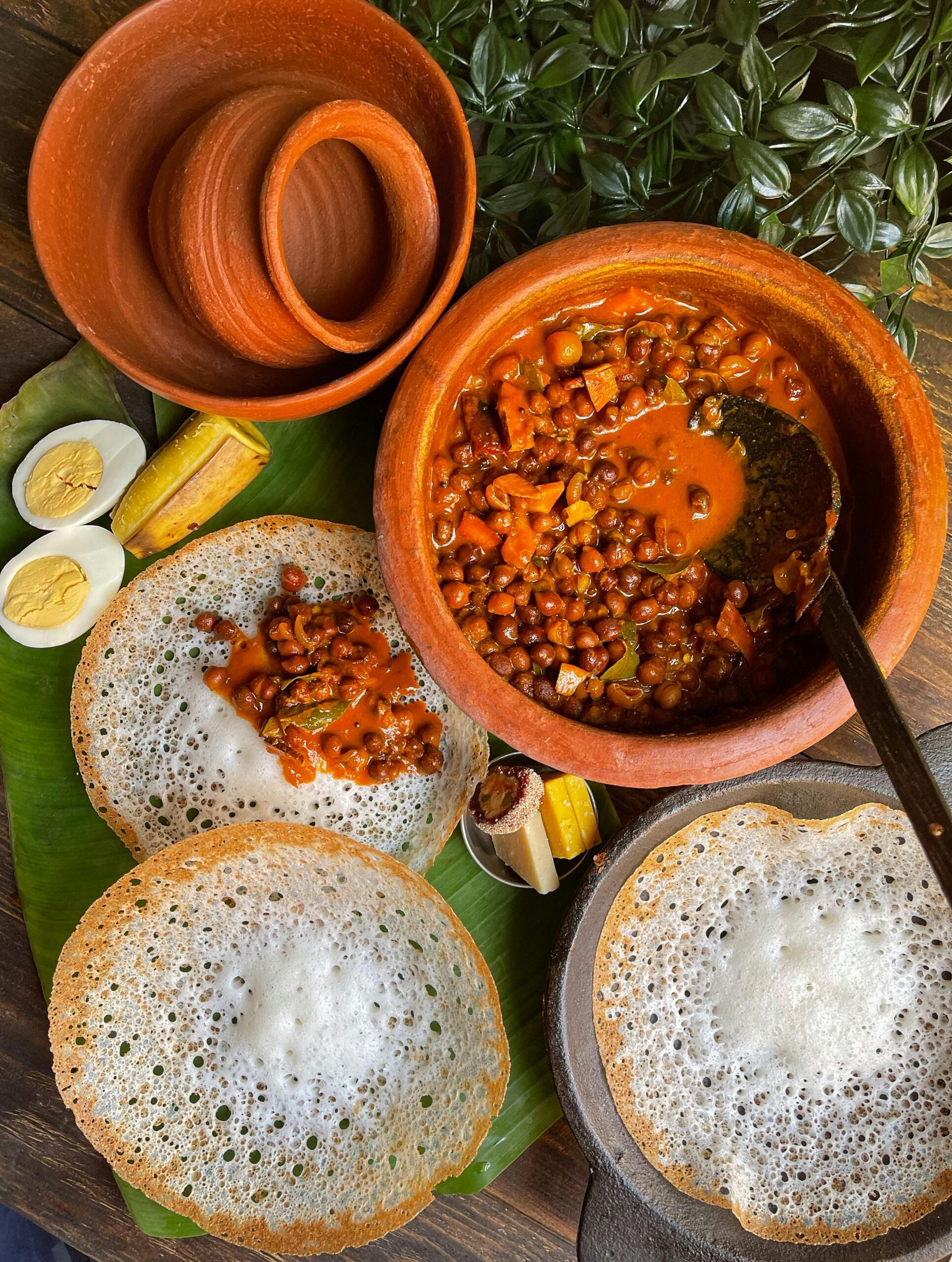 Delicious Kerala breakfast featuring appam, spicy curry, boiled eggs and banana slices served on banana leaf.